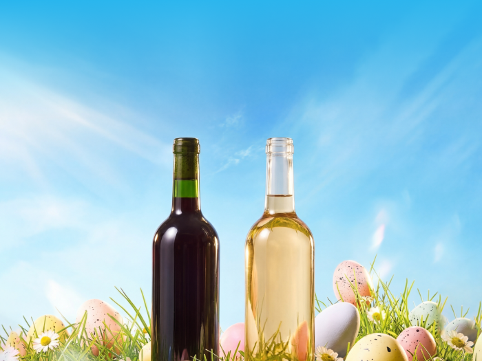 two bottles of wine and easter eggs in a a grassy field with blue sky