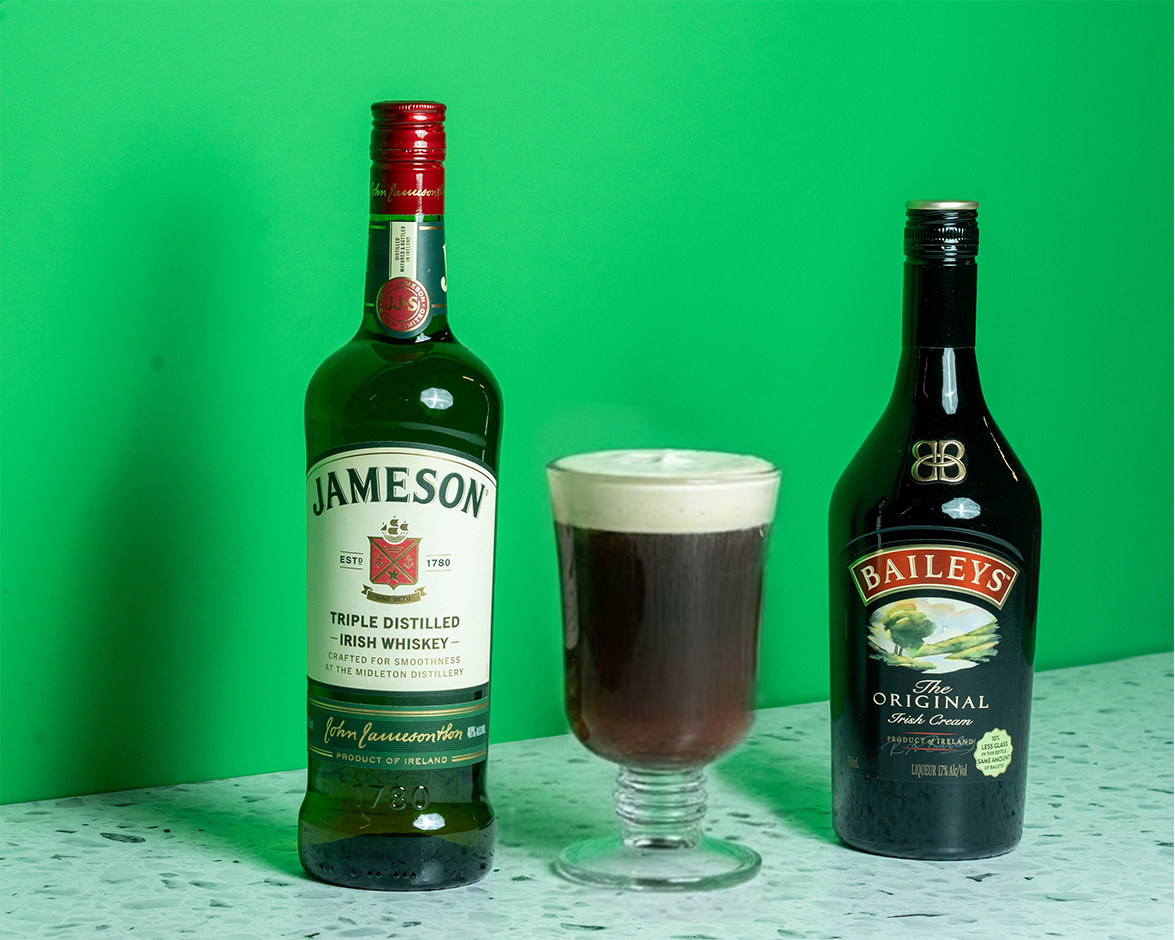 A bottle of Jameson, a bottle of Bailey's, and an Irish Coffee on a green background.