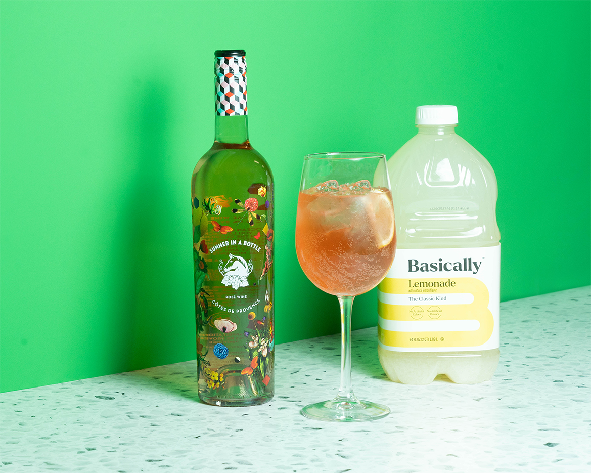 Bottles of rose wine and lemonade with a cocktail in a wine glass on a green background.